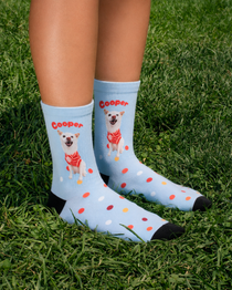 Pale blue crew socks with confetti dots, a dog printed on the leg and the name Cooper arched above, worn on grass